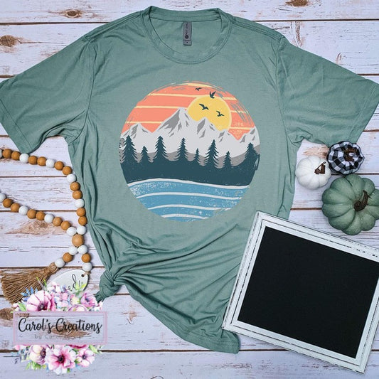 Green t-shirt with a scenic design on a wooden surface with decorative items.