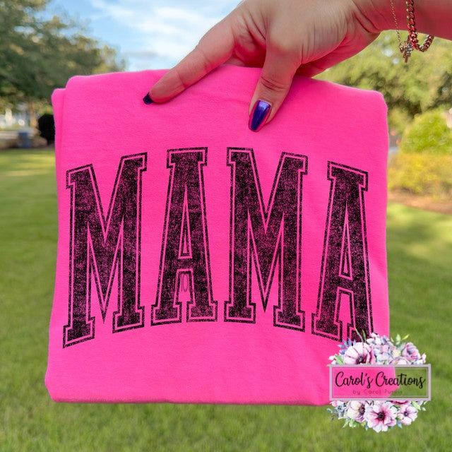 Pink fabric with 'MAMA' printed on it held by a hand outdoors.