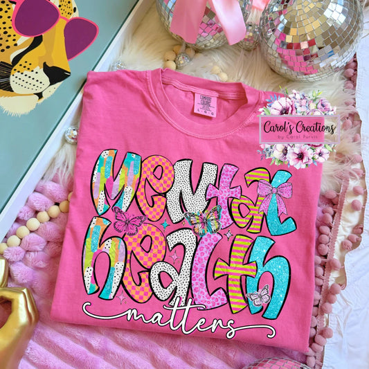 Pink t-shirt with colorful text and graphics on a decorative surface