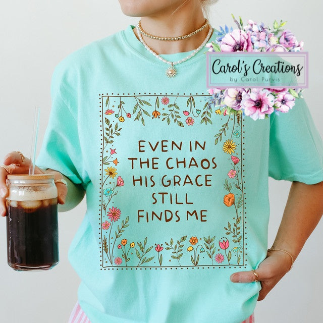 Person wearing a teal t-shirt with floral design and text, holding a drink.