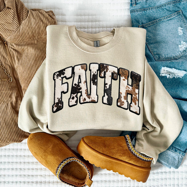 Beige sweatshirt with 'FAITH' print, paired with brown boots and jeans on a textured surface.