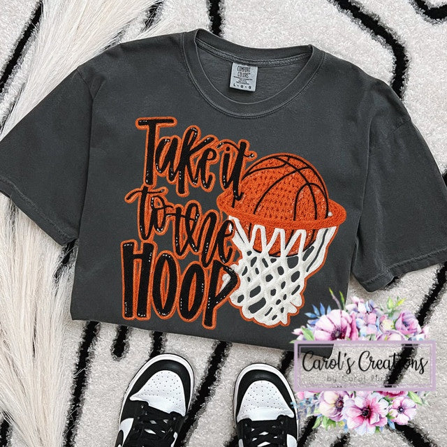 Gray t-shirt with basketball graphic and text 'Take it to the Hoop' on a textured surface.