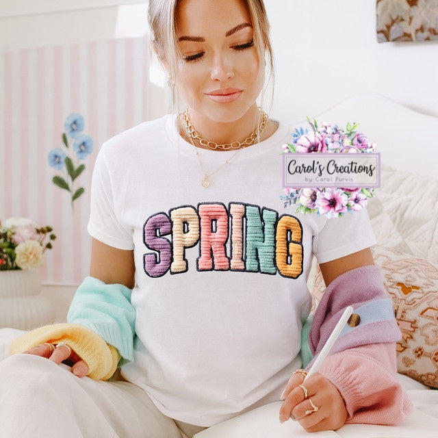 Woman wearing a white shirt with 'SPRING' in colorful letters, sitting on a couch.