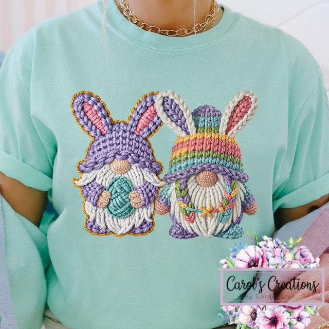 Light blue t-shirt with embroidered gnomes wearing rainbow hats, held by a person.