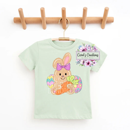 Light green t-shirt with a bunny design hanging on a wooden rack.