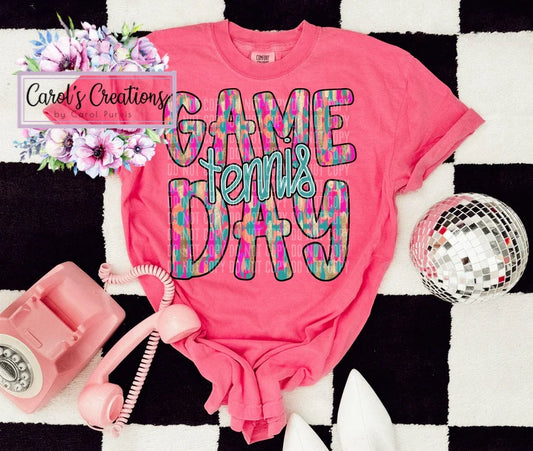 Pink t-shirt with 'Game Tennis Day' text on a black and white checkered background with decorative items.