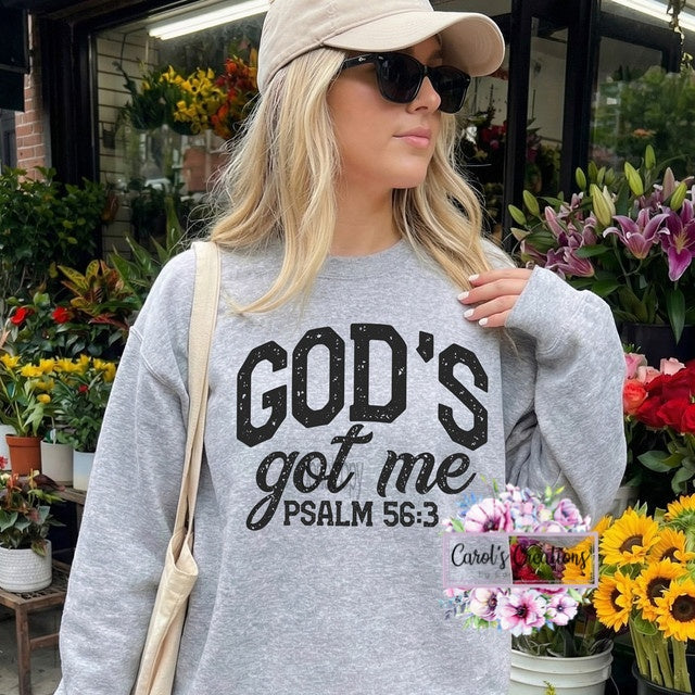 Woman wearing a gray sweatshirt with 'GOD'S got me PSALM 56:3' text, standing in a flower shop.