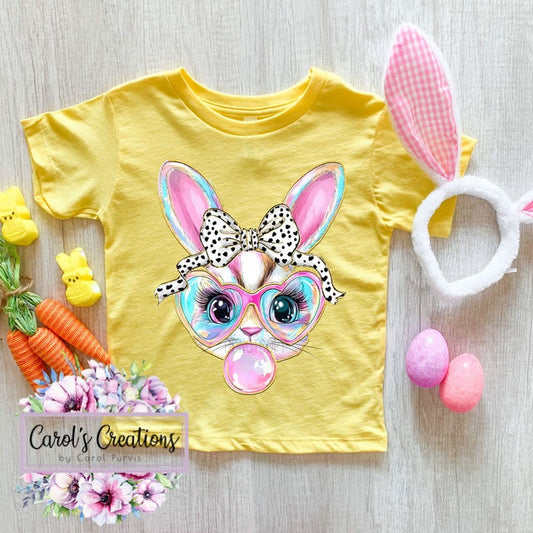 Yellow t-shirt with a colorful bunny design, surrounded by Easter-themed items on a wooden surface.