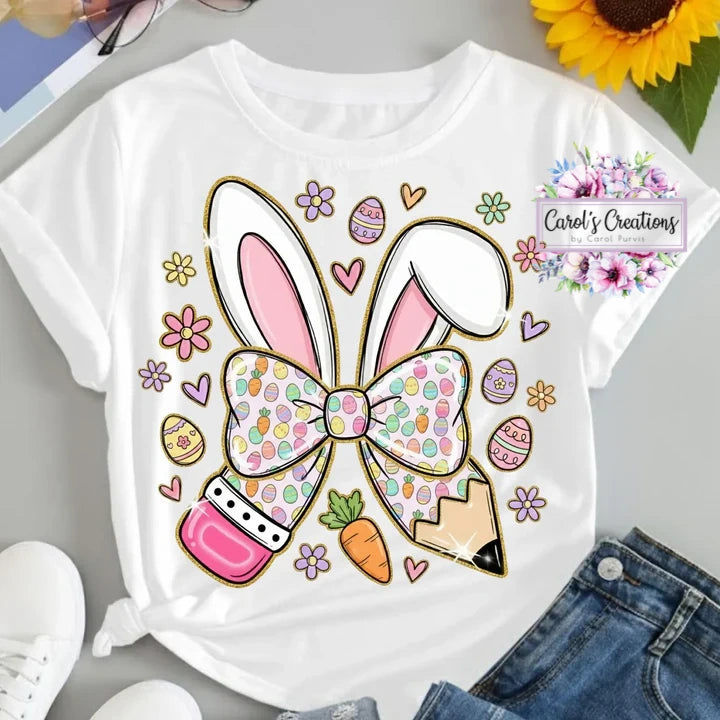 White t-shirt with a colorful bunny bow design on a gray surface with denim jeans and a sunflower.