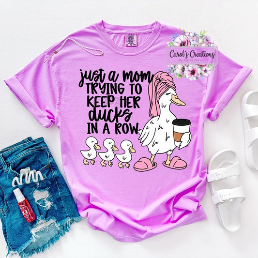 Pink t-shirt with a graphic and text, paired with denim shorts and white sandals on a light background.