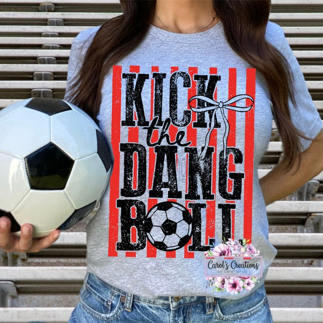 Person wearing a t-shirt with 'Kick the Dang Ball' design holding a soccer ball.