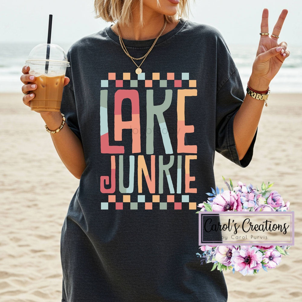 Person wearing a 'Lake Junkie' t-shirt on a beach, holding a drink.