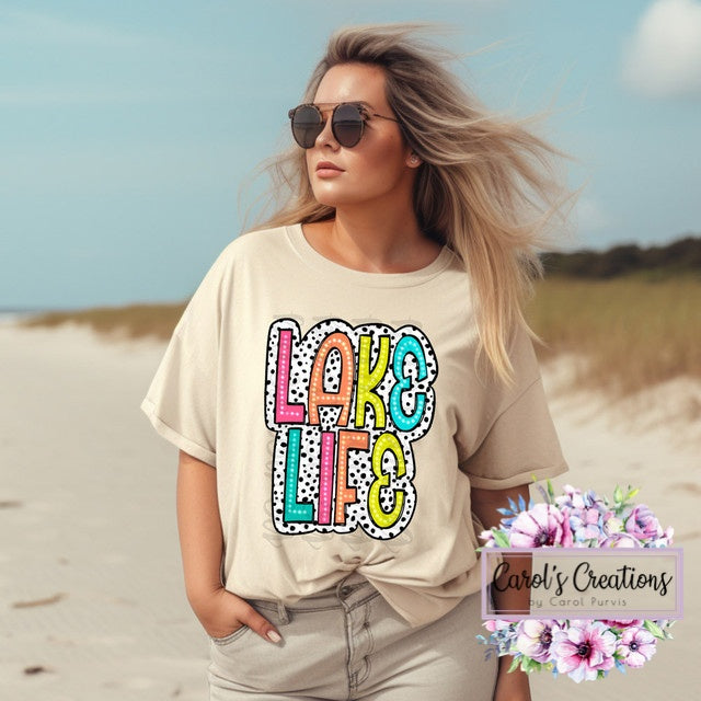 Woman wearing a 'Lake Life' t-shirt on a beach with 'Carol's Creations' branding.