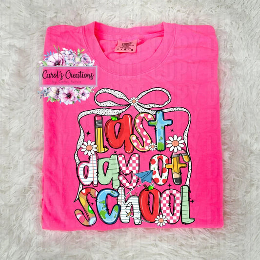 Pink t-shirt with 'Last Day of School' design on a textured surface