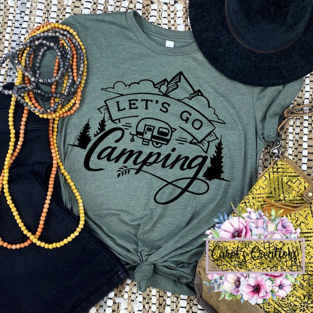 Green t-shirt with 'Let's Go Camping' design, surrounded by camping-themed accessories on a woven surface.