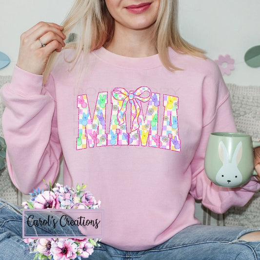 Person wearing a pink sweatshirt with colorful 'Mama' design, holding a green mug with a bunny design.