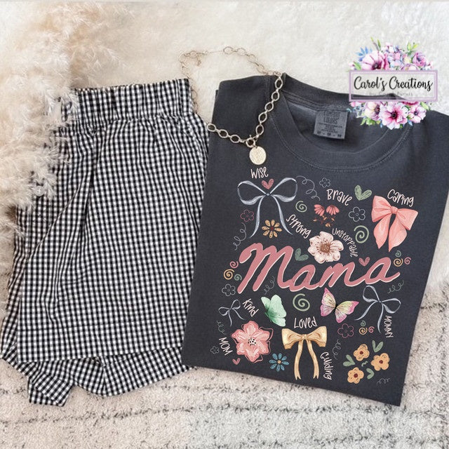 Black t-shirt with 'Mama' design, black checkered shorts, and necklace on a textured surface.
