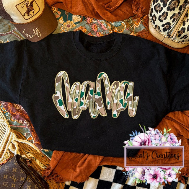 Black sweatshirt with 'Mama' in floral letters on a patterned surface.