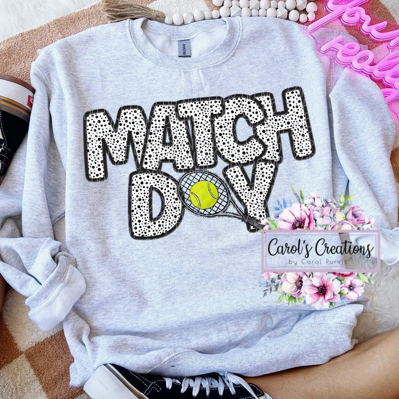 Gray sweatshirt with 'MATCH DAY' text and tennis graphics, displayed on a surface.