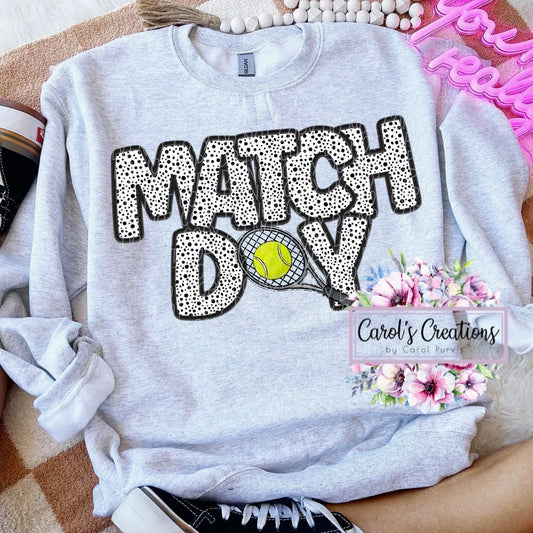 Gray sweatshirt with 'MATCH DAY' text and tennis graphics, displayed on a surface.