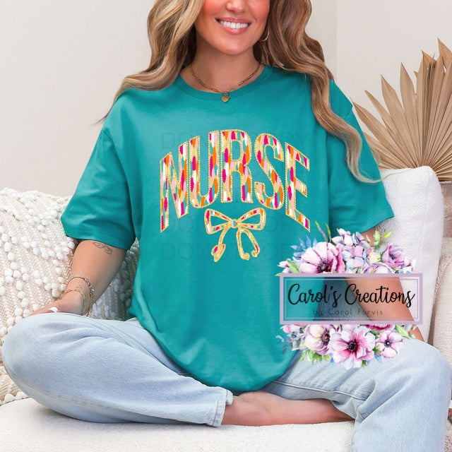 Person wearing a teal 'NURSE' shirt with colorful design, sitting on a couch.