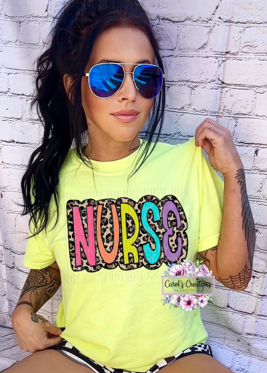 Woman wearing a bright yellow t-shirt with 'NURSE' printed on it, sunglasses, and floral accessories against a white brick wall.