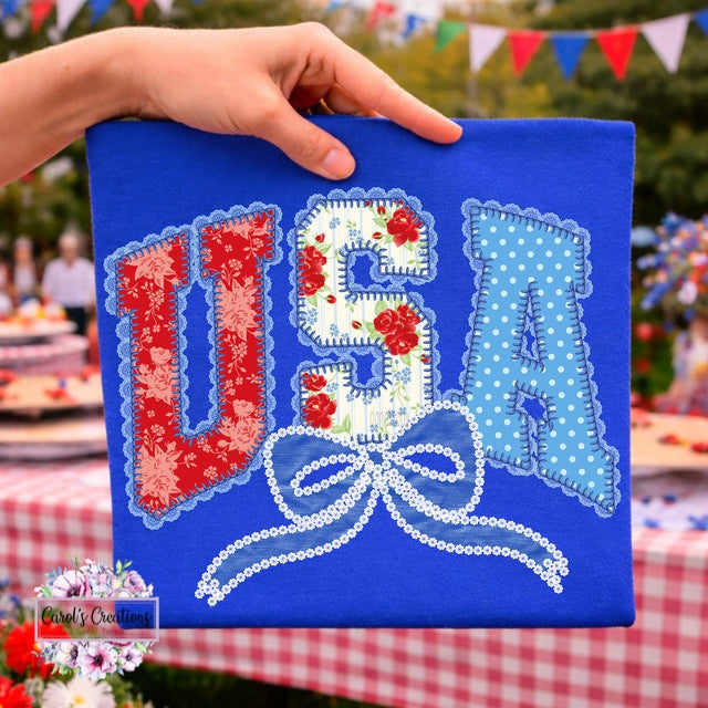 Hand holding a blue canvas with 'USA' text in floral and polka dot patterns, outdoor setting with flags.