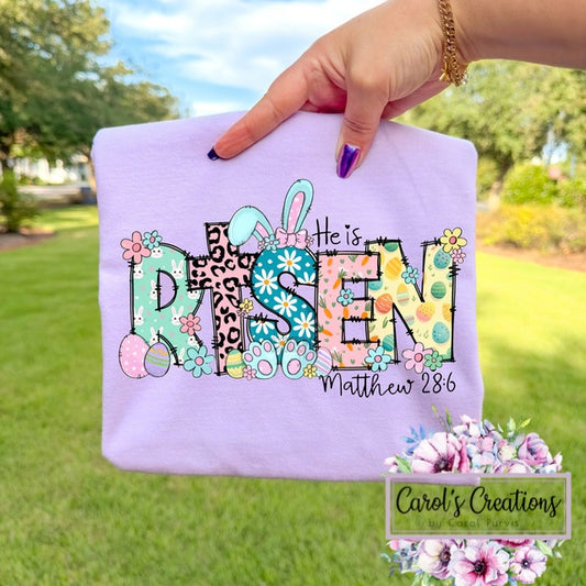 Hand holding a purple pillow with 'He is Risen' text and Easter elements, outdoors.