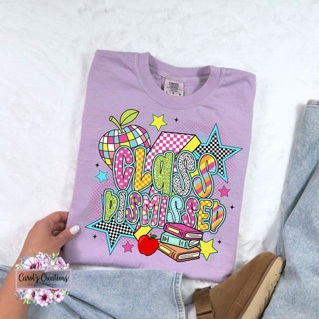 Folded purple sweatshirt with 'Class Dismissed' design held by a hand on a light background