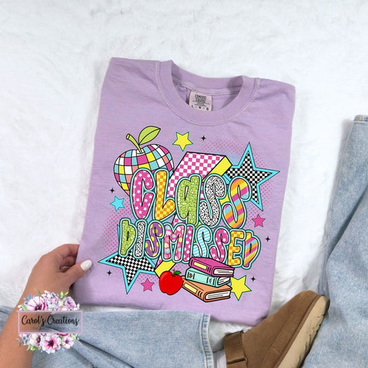 Folded purple sweatshirt with 'Class Dismissed' design held by a hand on a light background