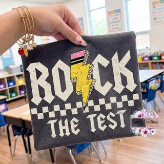 Black pouch with 'Rock the Test' design held by a hand in a classroom setting