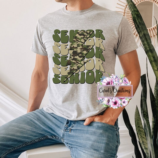 Person wearing a gray t-shirt with 'Senior 2023' design, sitting indoors.