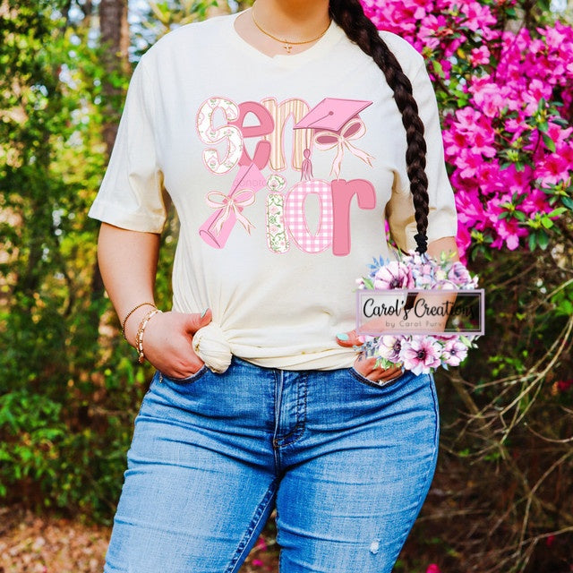 Person wearing a white t-shirt with pink and red text, standing outdoors with pink flowers in the background.
