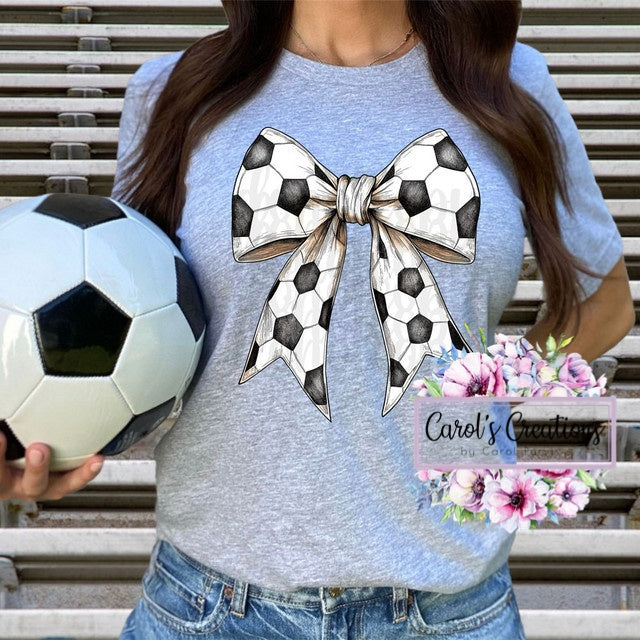 Person wearing a blue t-shirt with a soccer ball and bow design, holding a soccer ball and flowers.