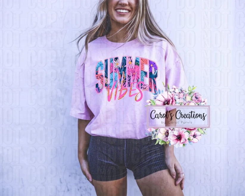 Woman wearing a pink 'Summer Vibes' shirt with floral graphics, standing against a light blue textured background.