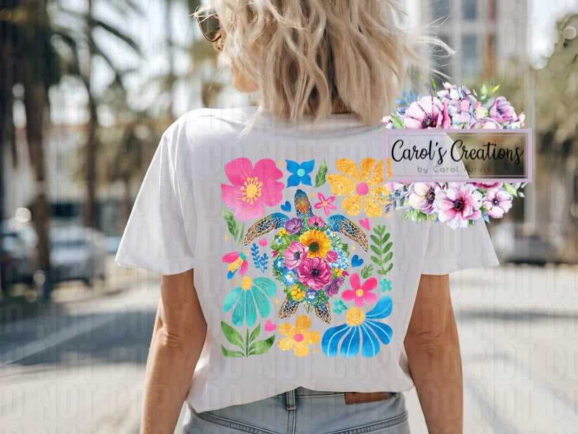 Person wearing a white t-shirt with colorful floral and turtle design, standing outdoors.