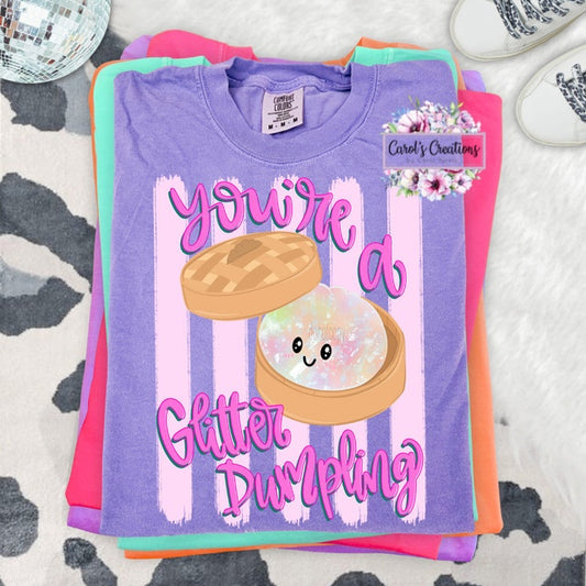 Stack of colorful t-shirts with a purple shirt featuring a 'Glitter Dumpling' design.